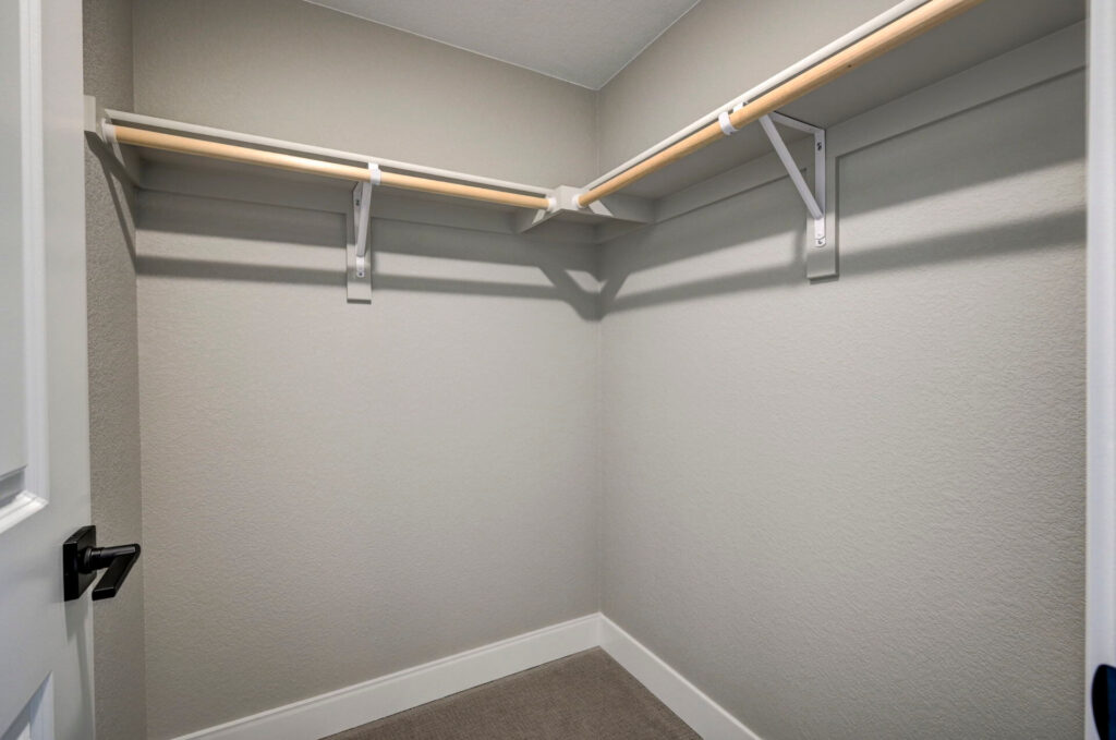Small walk-in closet with L-shaped wood hanging rods and shelf supports.