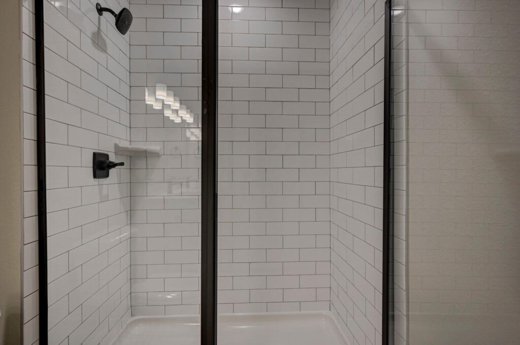 Close-up of a glass-enclosed shower with white subway tile and dark fixtures.