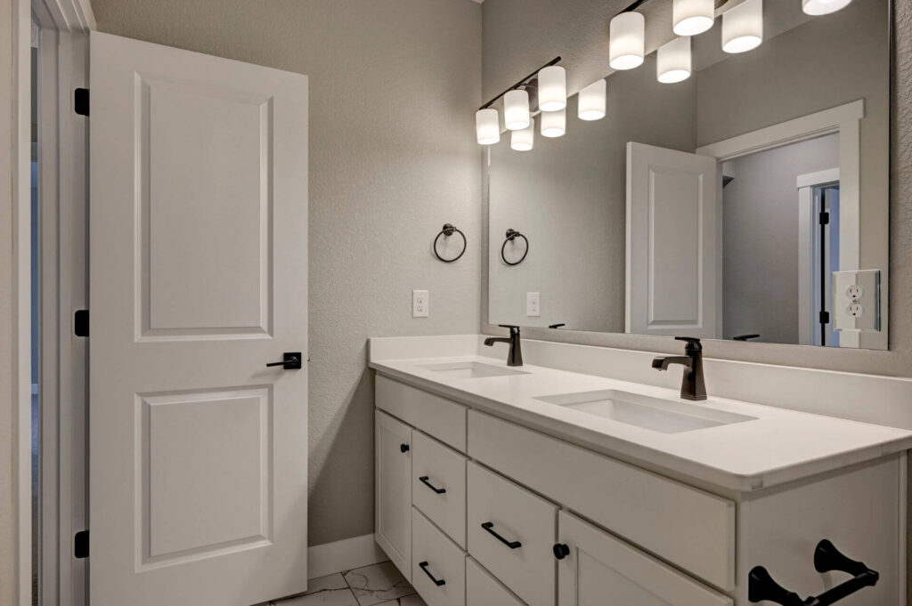 Double-sink vanity and large mirror with modern three-light fixtures in a neutral bathroom.