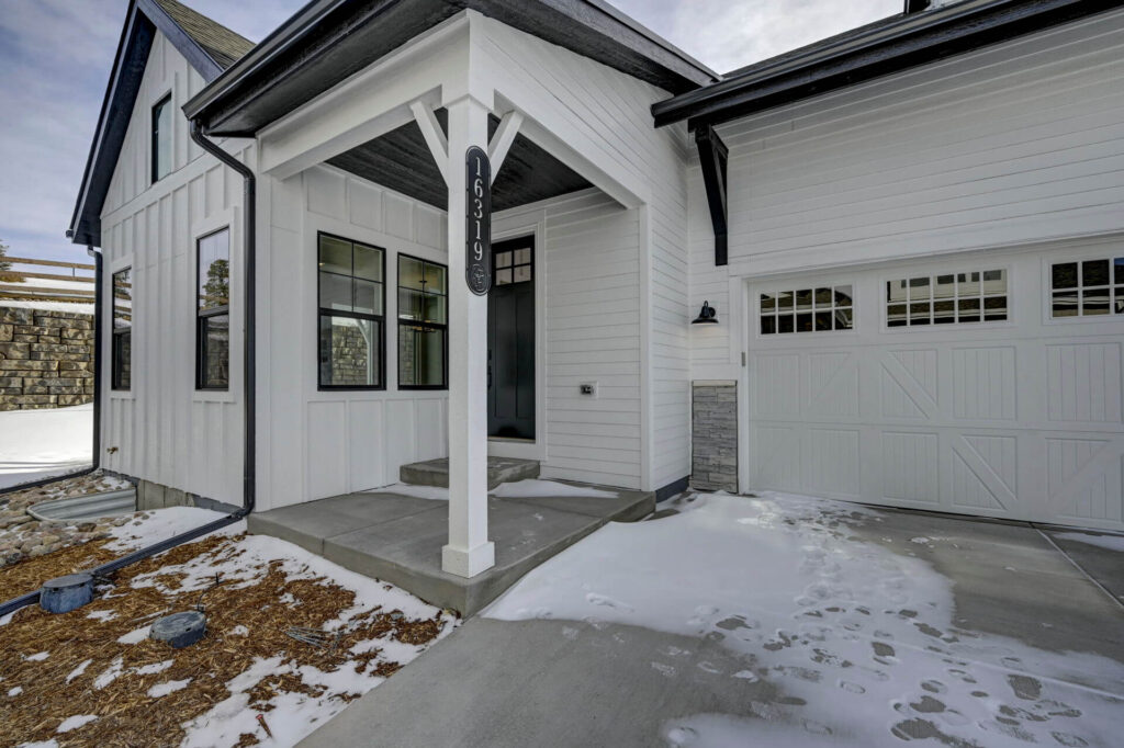 Front entry porch and attached garage of a white house with snow on driveway.