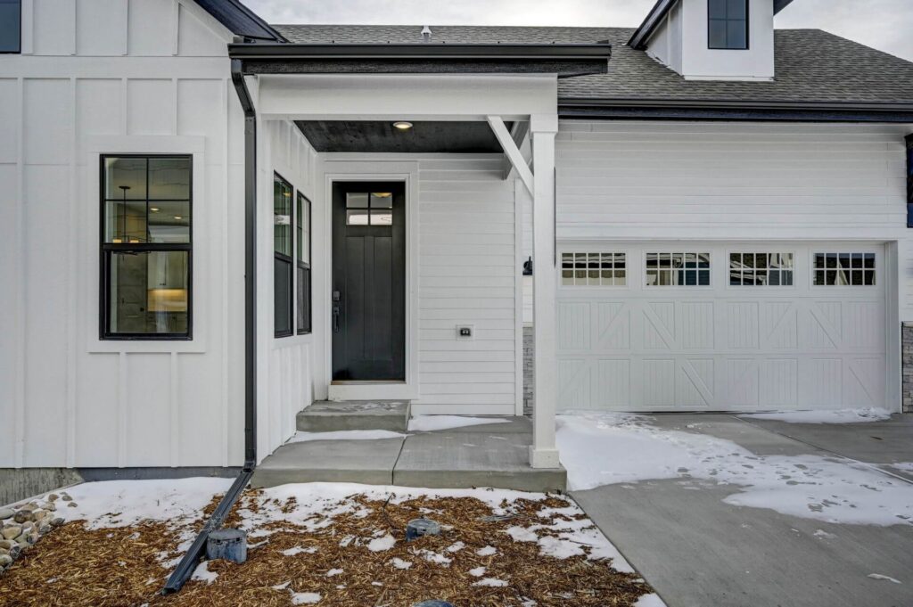 Front entry of a white modern farmhouse with black door, single-column porch, and attached garage.