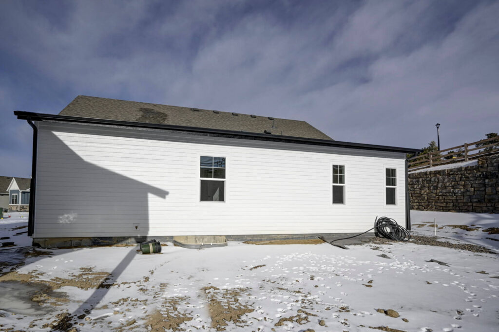 Side wall of a white single-story house with three windows and snow on the ground.