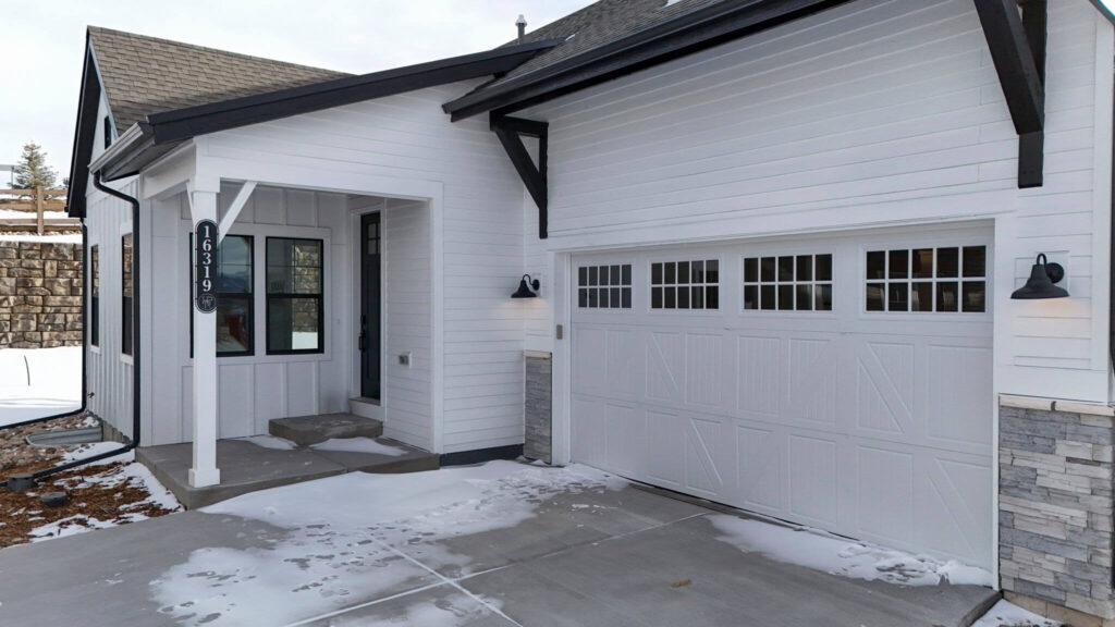 Front entry and attached two-car garage of a white house with black trim, light dusting of snow.
