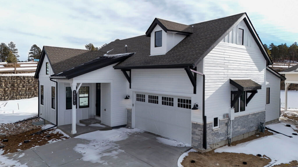 Angled front exterior of a white house with black roof accents and snow-covered ground.