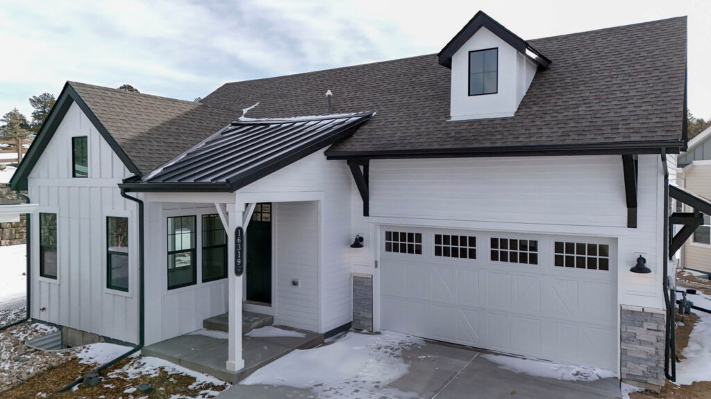Front-right view of a white home featuring a covered entry with metal awning and garage.