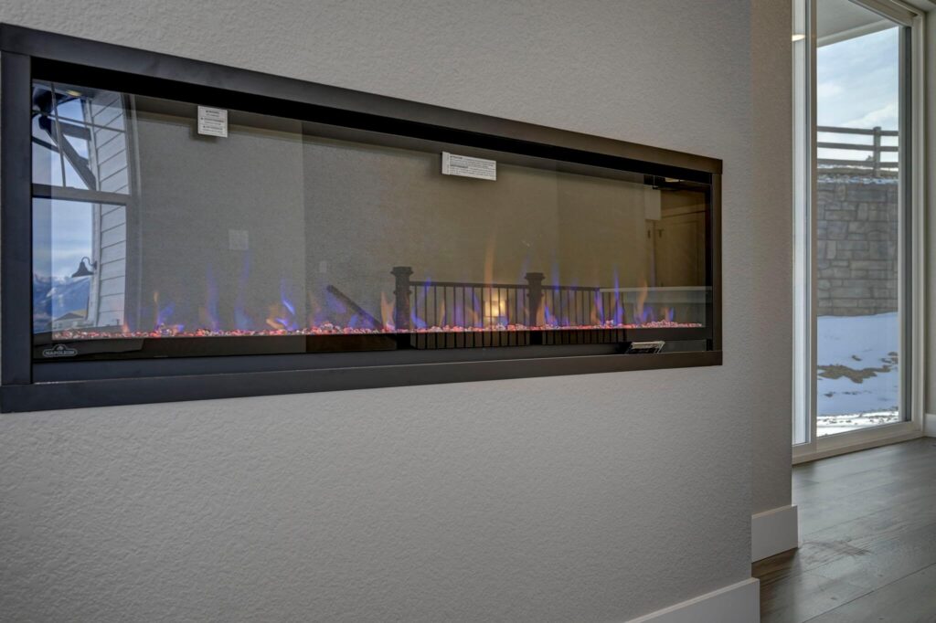 Long rectangular built-in linear fireplace with blue-orange flames in a wall opening.