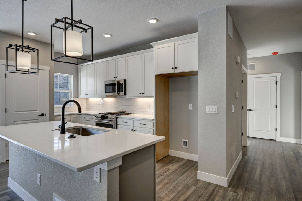 Modern kitchen with island, white cabinets, waterfall countertop, and black pendant lights.