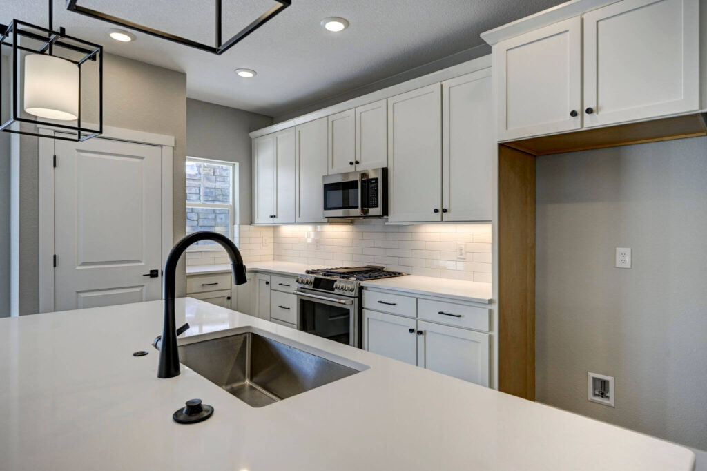 Close-up of kitchen island sink and faucet with white counters and cabinetry.