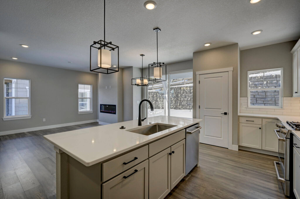 Kitchen island and open living area with pendant lights and large windows.