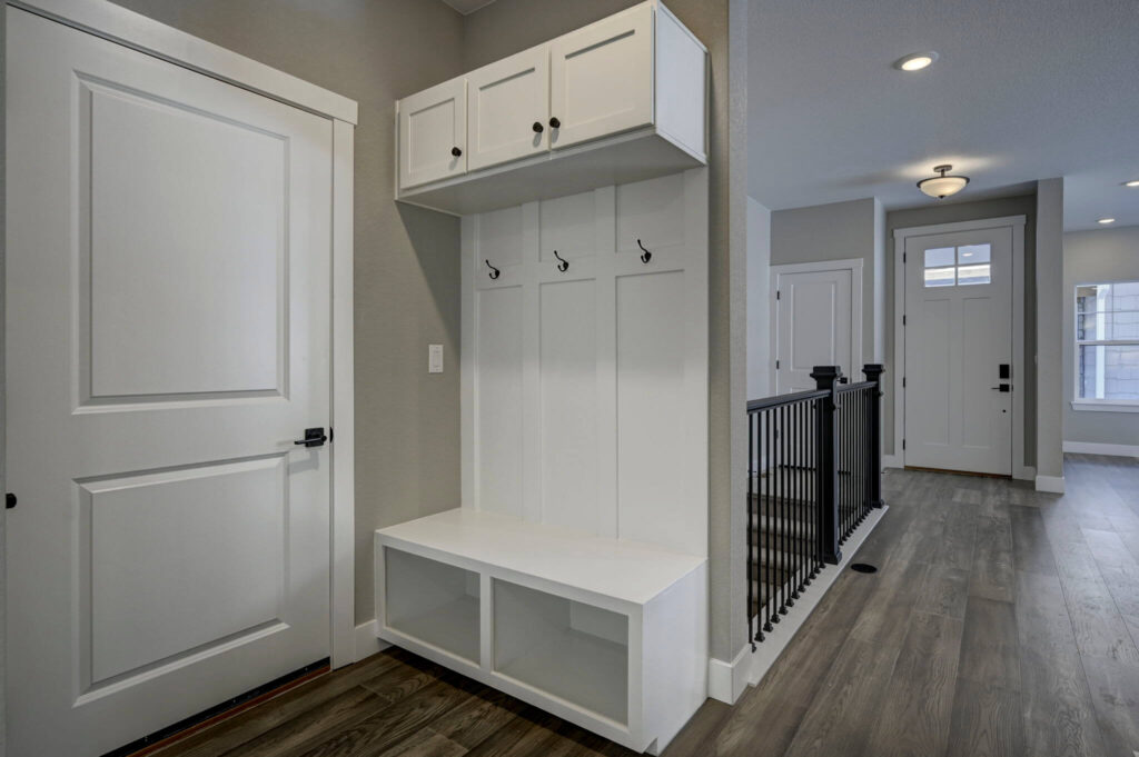 Mudroom bench with cubbies, coat hooks, upper cabinets and nearby hallway rail.
