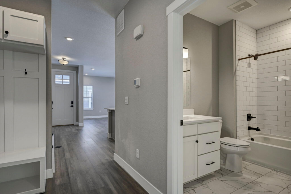 Hallway view into a bathroom with white vanity and tiled bathtub surround.
