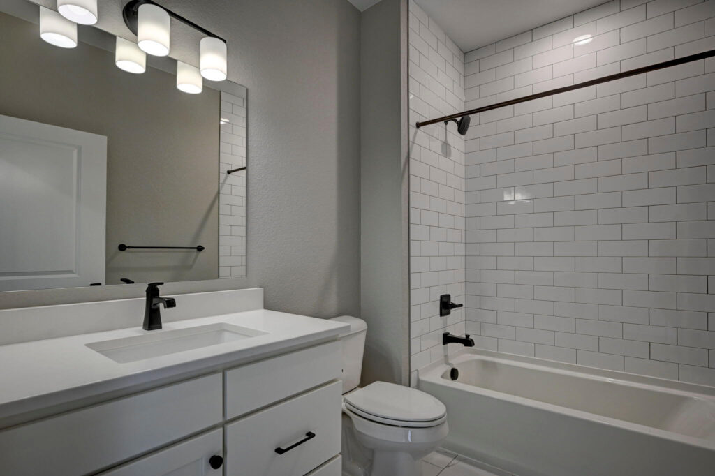 Modern bathroom with white vanity, toilet, and tiled tub-shower with black fixtures.