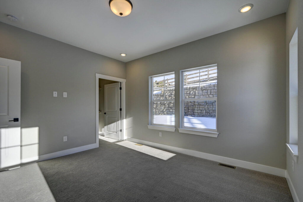 Empty bedroom with two windows, door to another room, and neutral paint and carpet.