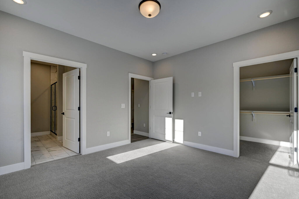 Empty carpeted bedroom with three open doors, neutral gray walls, and ceiling light.