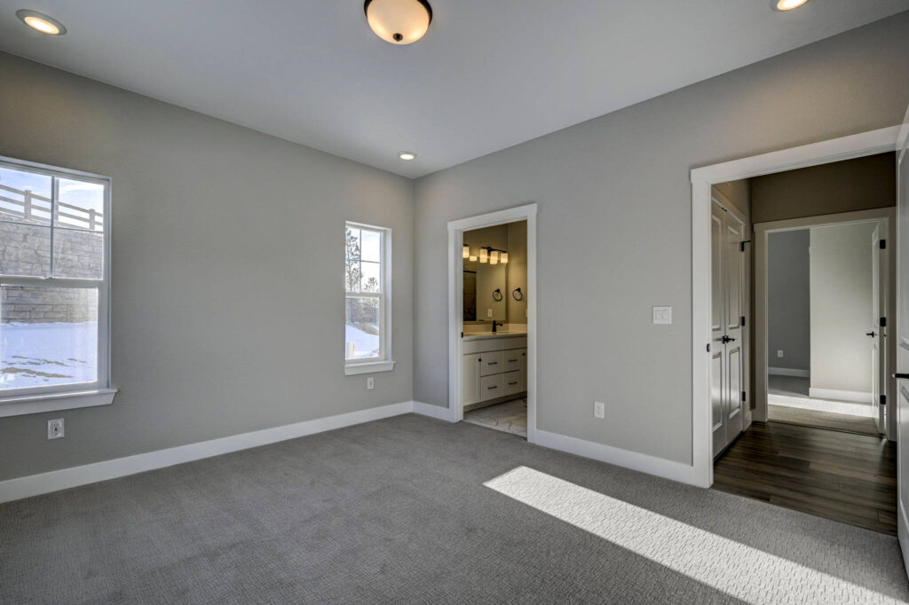 Well-lit empty bedroom with two windows, carpeted floor, and doorway to a vanity area.