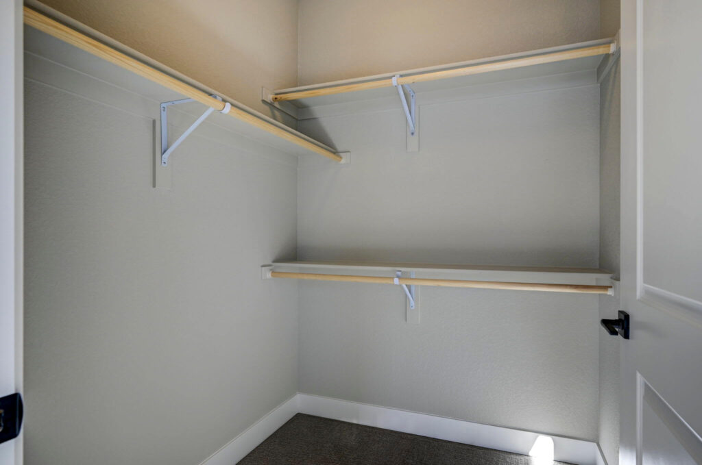 Small walk-in closet with multiple wooden hanging rods and light gray walls.