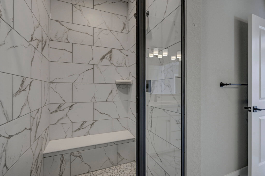 Tiled walk-in shower with built-in bench and pebble floor seen through a glass door.