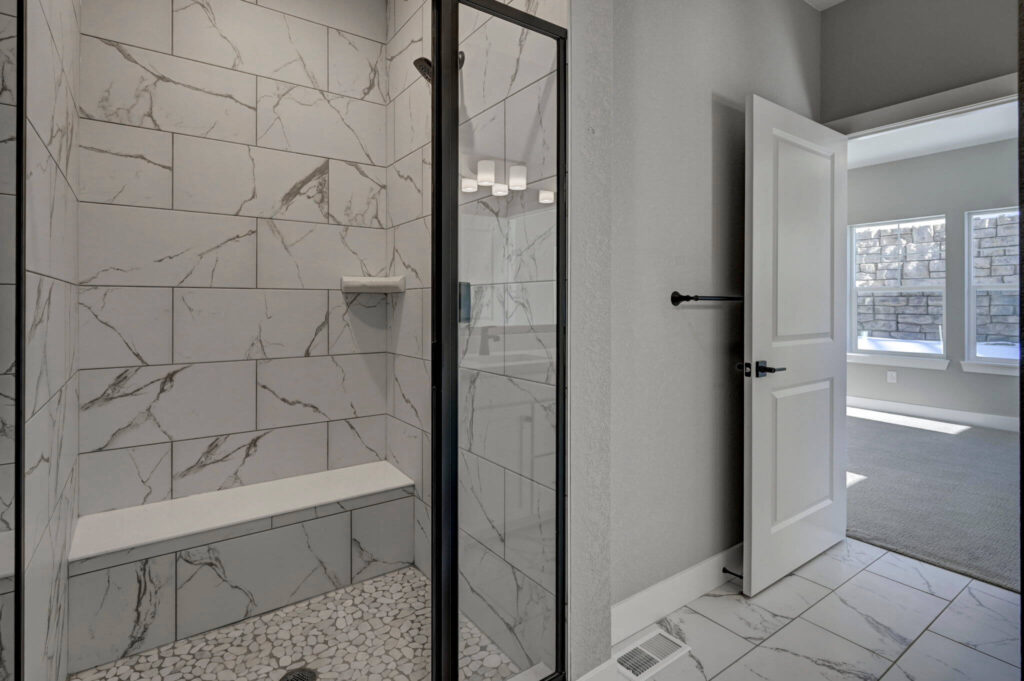 Bathroom doorway opening to a tiled shower with bench and a carpeted room beyond.
