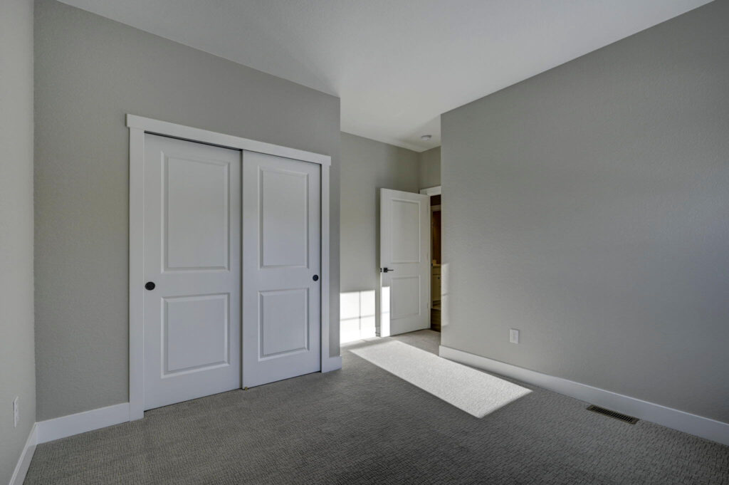 Carpeted room showing closed double closet doors and an open entry door with sunlight on the floor.
