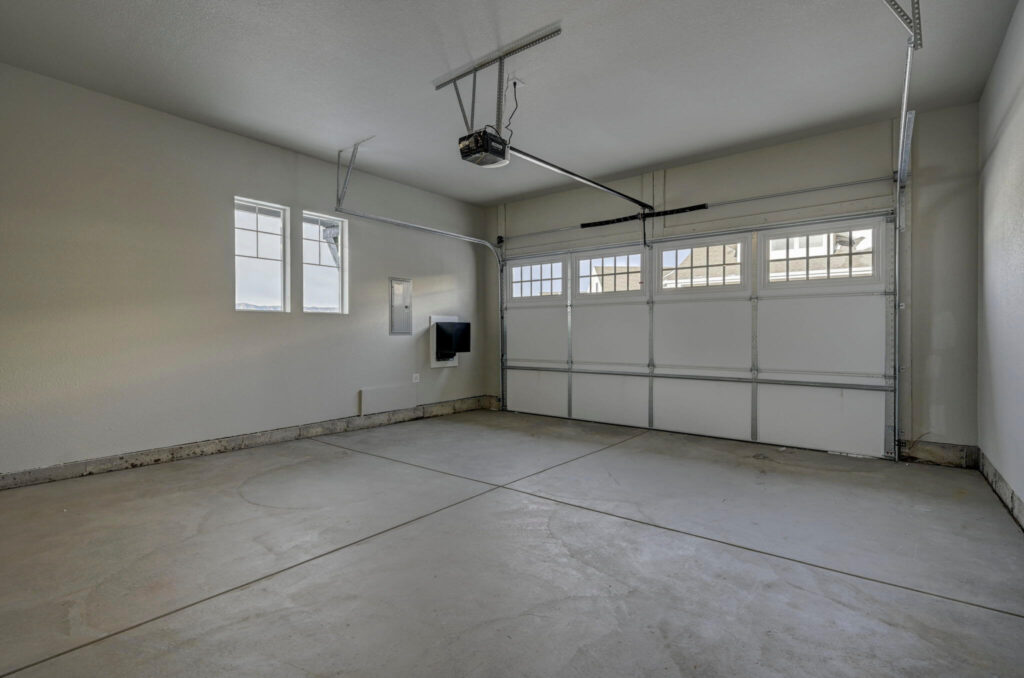 Two-car garage with concrete floor, automatic garage door and small windows on side wall.