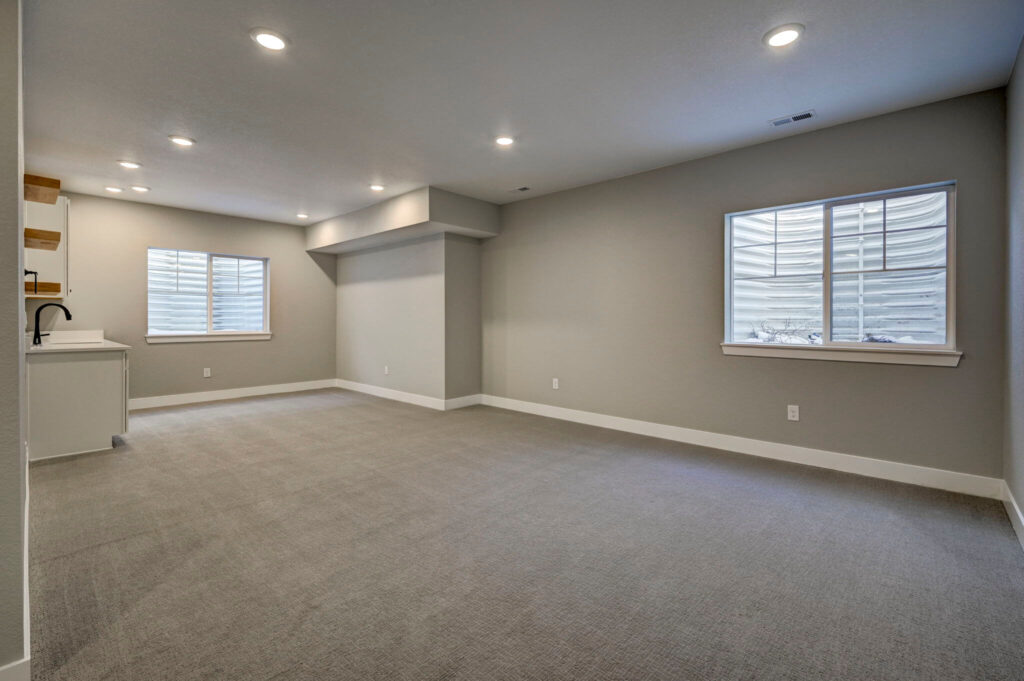 Large open finished basement room with two windows and built-in sink area on the left.