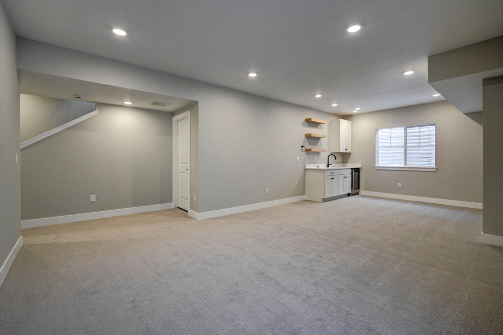 Open finished basement area with kitchenette, shelving, and recessed lighting.