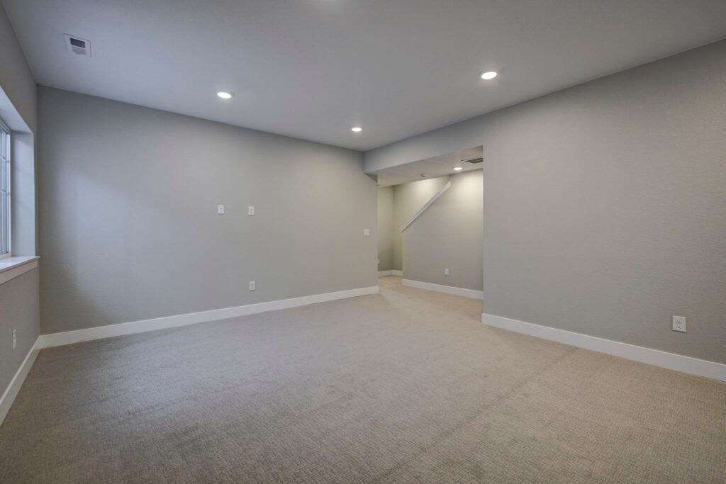 Empty finished basement room with recessed lights, beige carpet, and a window on the left wall.