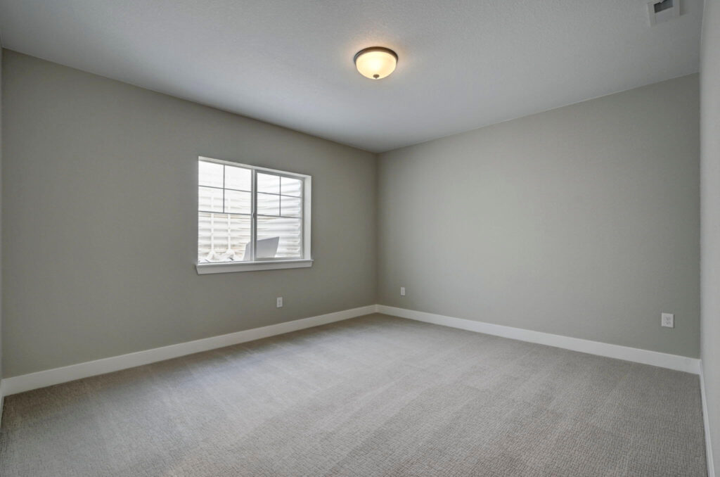 Empty carpeted bedroom or bonus room with a single window and flush ceiling light