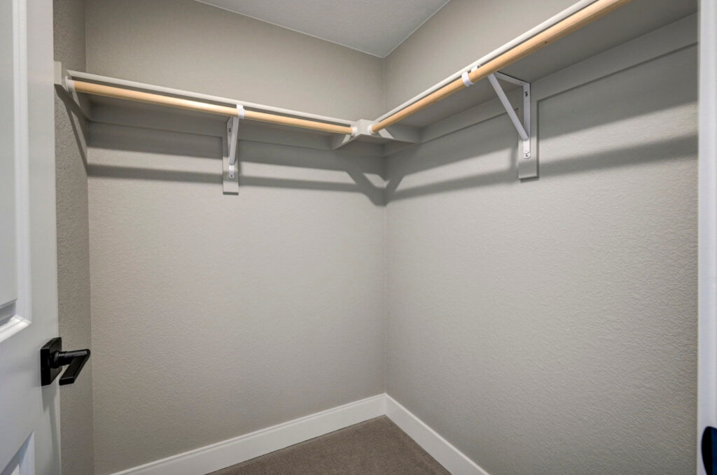 Small walk-in closet with L-shaped wooden hanging rods and shelf supports