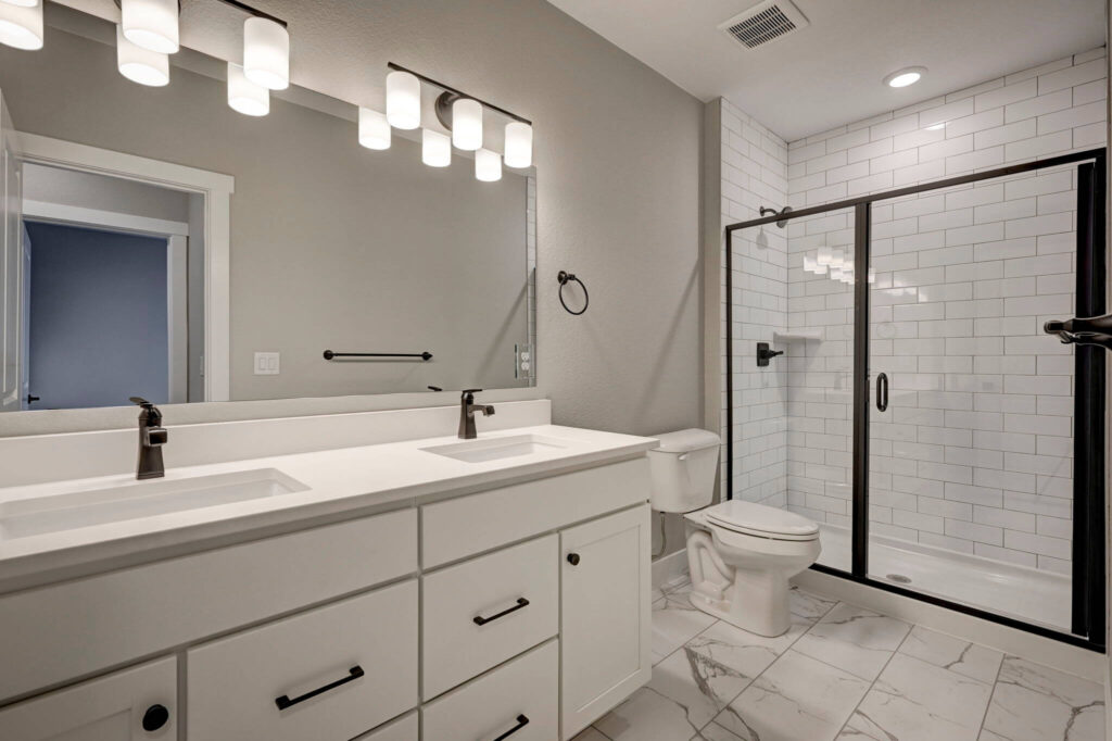 Bathroom with double-sink vanity, large mirror, toilet, and glass-enclosed tiled shower.