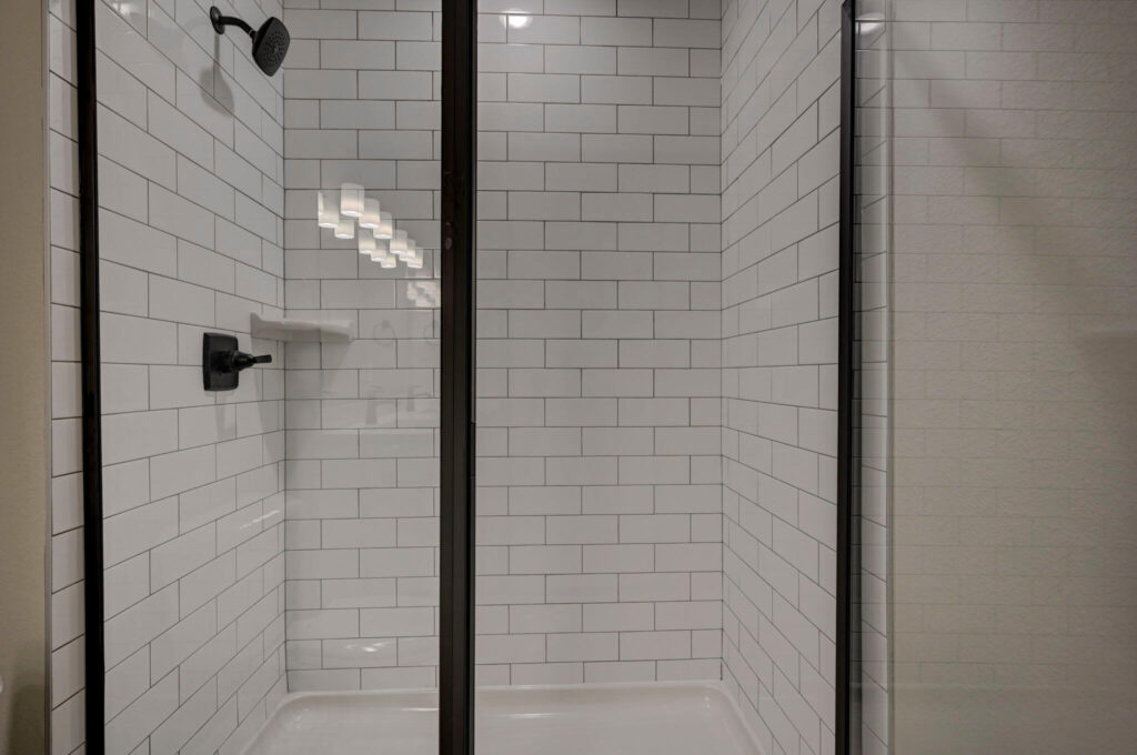 Glass shower with white subway tile walls and dark metal frame and fixtures.
