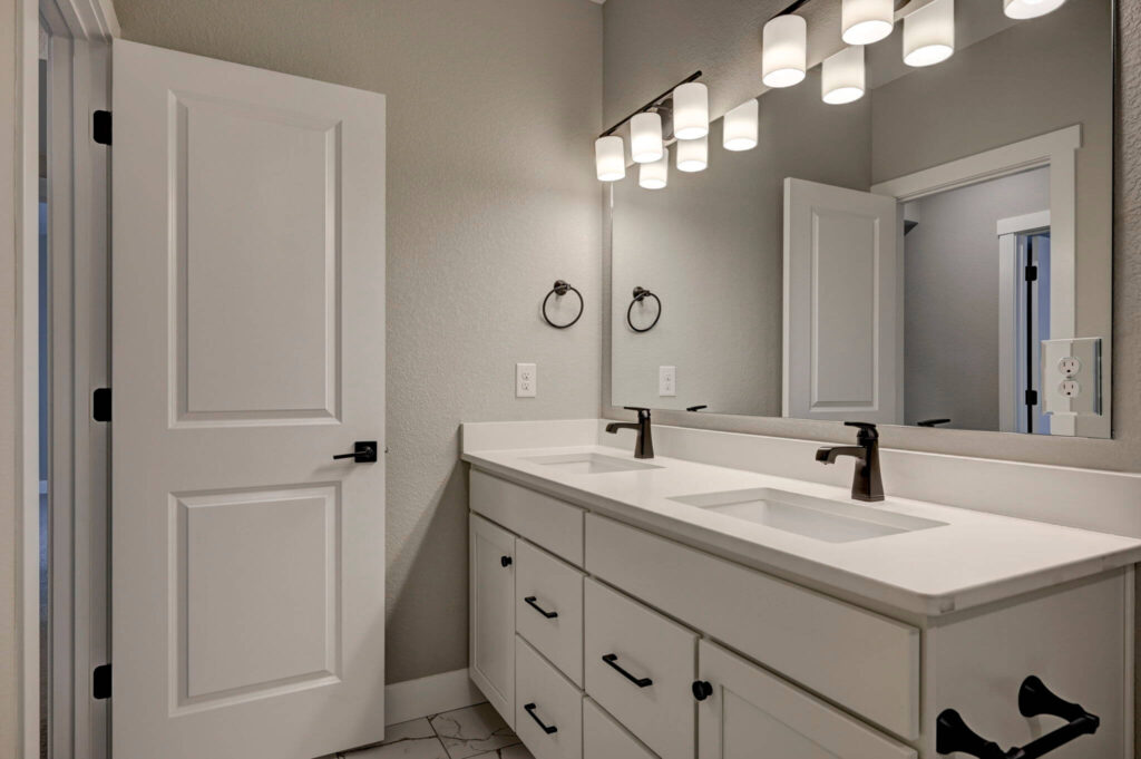 Double-sink vanity with white cabinets, large mirror, and overhead vanity lights.