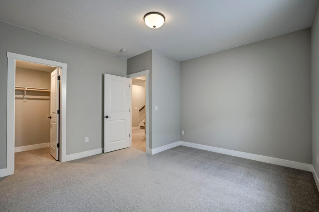 Empty bedroom with carpet, light-gray walls, closet and an open door leading to a staircase.