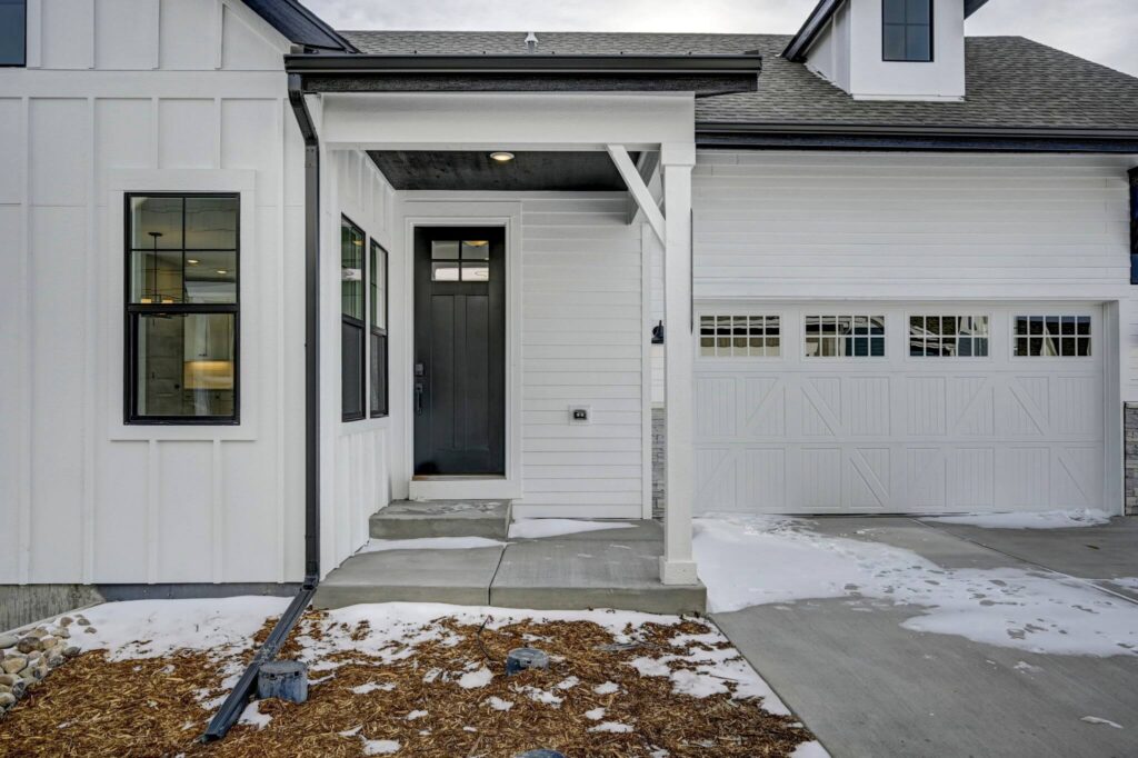 Front entry of a white modern farmhouse with covered porch, black door, and adjacent garage door.