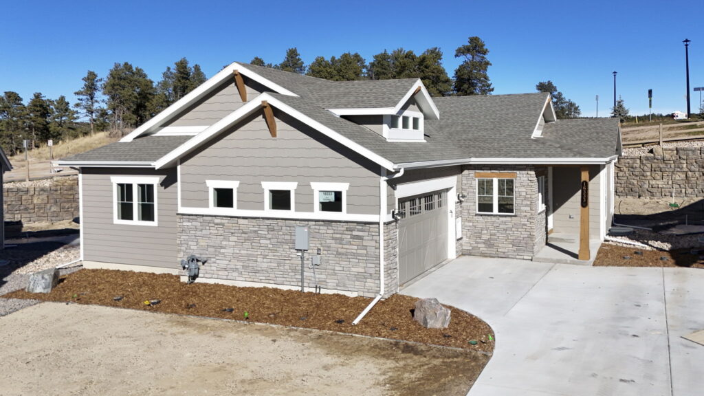 Single-story gray house exterior with stone accents and attached two-car garage under clear sky.