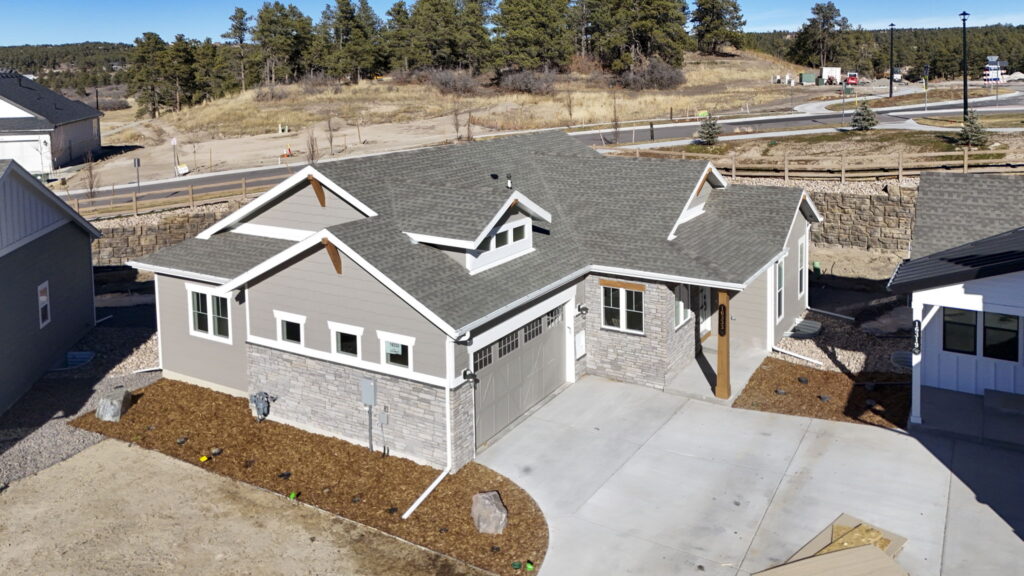 Aerial angled view of the same gray house showing rooflines, garage, and surrounding lots.