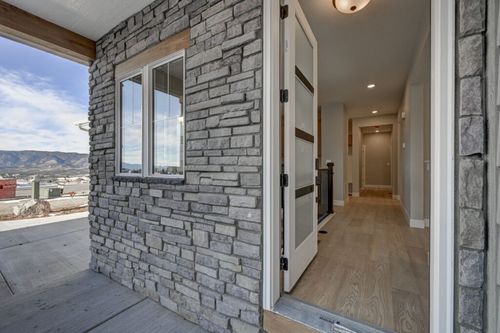 Open front door revealing a stone-clad porch wall and an interior hallway with wood flooring.