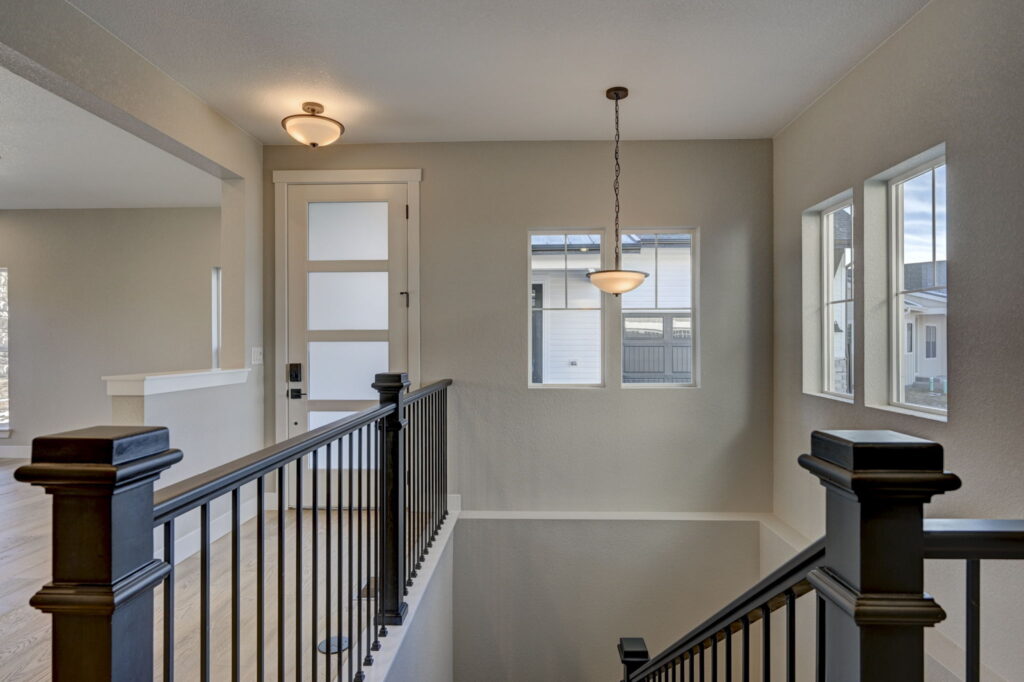 Top of staircase with black metal balustrade, frosted front door and pendant light.