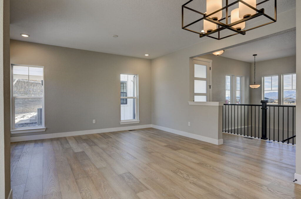 Open room with pale wood floors, two narrow windows, and a view to a stair railing and entry area.