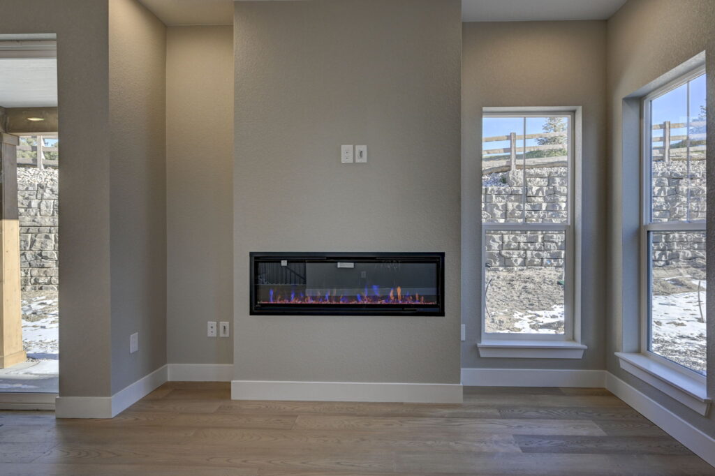 Modern living area wall with a linear gas fireplace flanked by tall windows and light wood floors.
