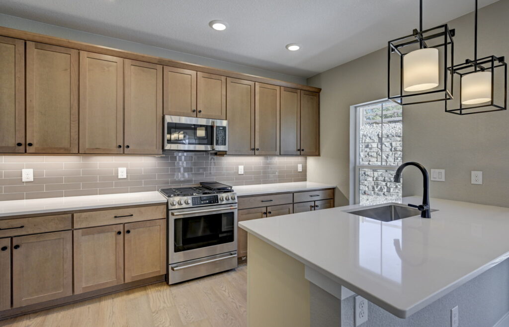 Modern kitchen with light wood cabinets, stainless range and island with black faucet.