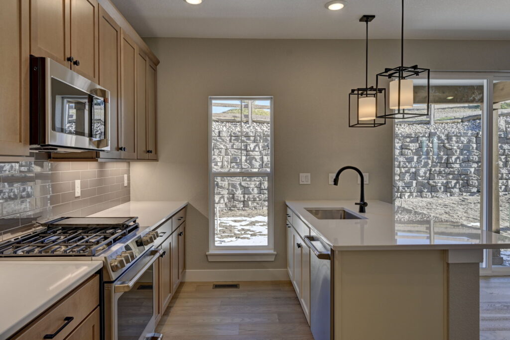 Kitchen aisle with stovetop, sink island, narrow window and sliding glass door beyond.