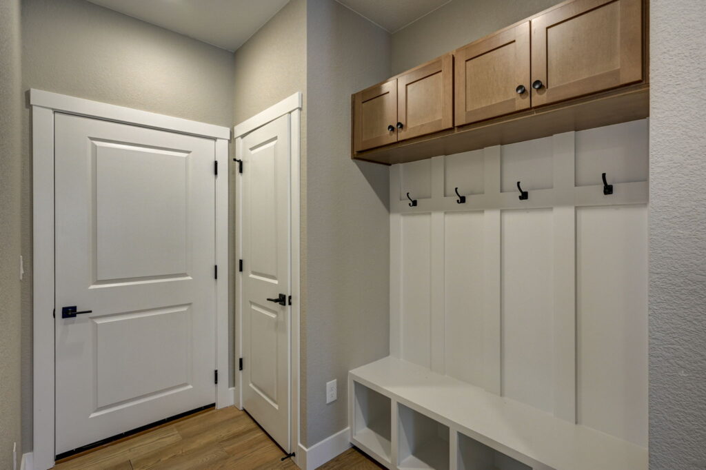 Entryway mudroom bench with cubbies, coat hooks, and upper cabinets beside two white doors.