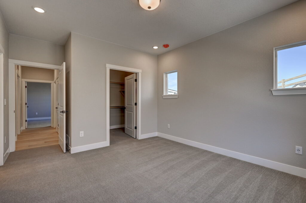 Empty carpeted bedroom with two small windows and open closet door under soft ceiling lights.