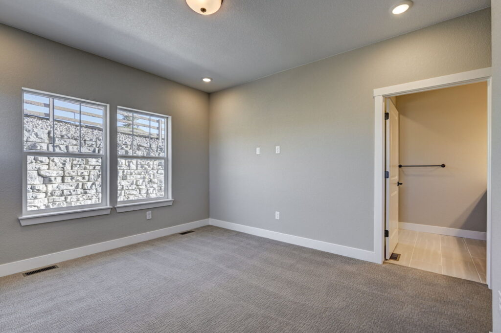 Bright empty bedroom with large double window and doorway to a tiled bathroom or closet area.