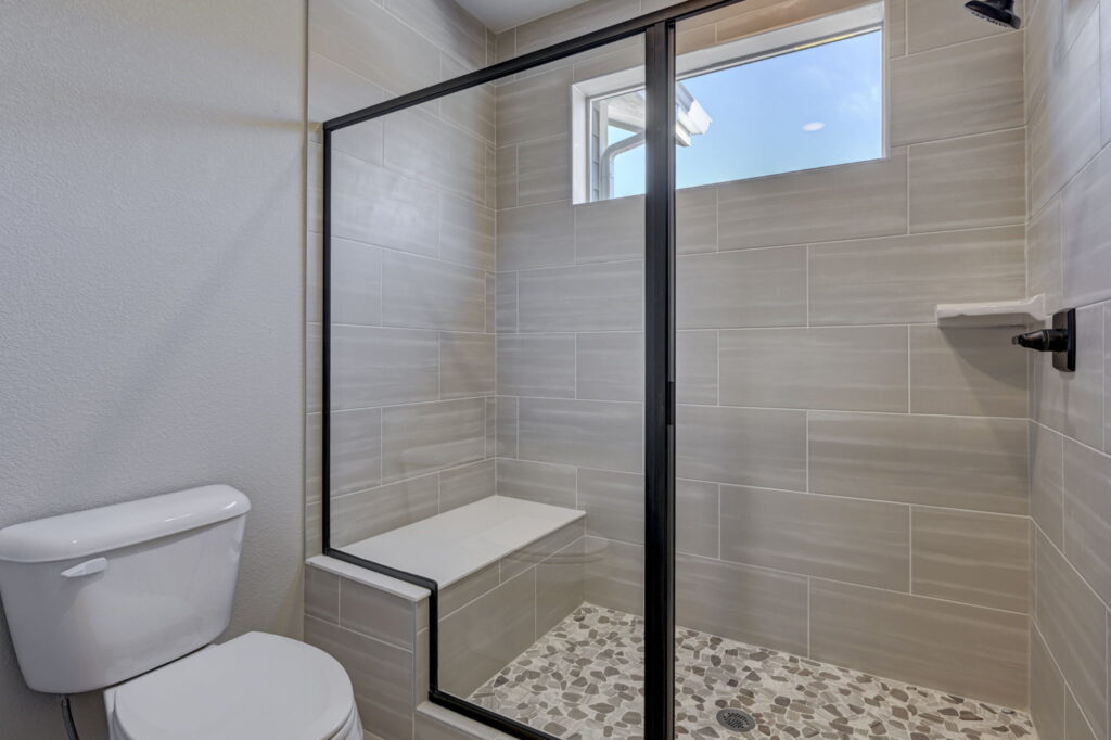 Walk-in tiled shower with glass door, built-in bench, pebble-style floor and small high window