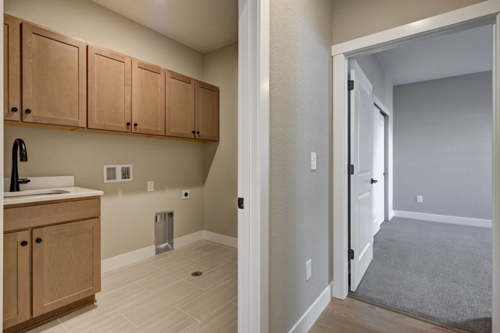 Laundry room with upper wood cabinets, utility sink, and open doorway to a carpeted room