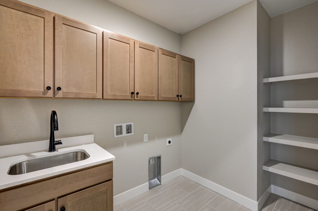 Laundry room with upper cabinets, sink, open shelving and washer/dryer hookups.