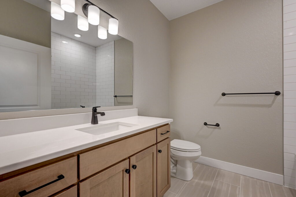 Bathroom vanity with large mirror, single sink, wood cabinets and toilet beside it.