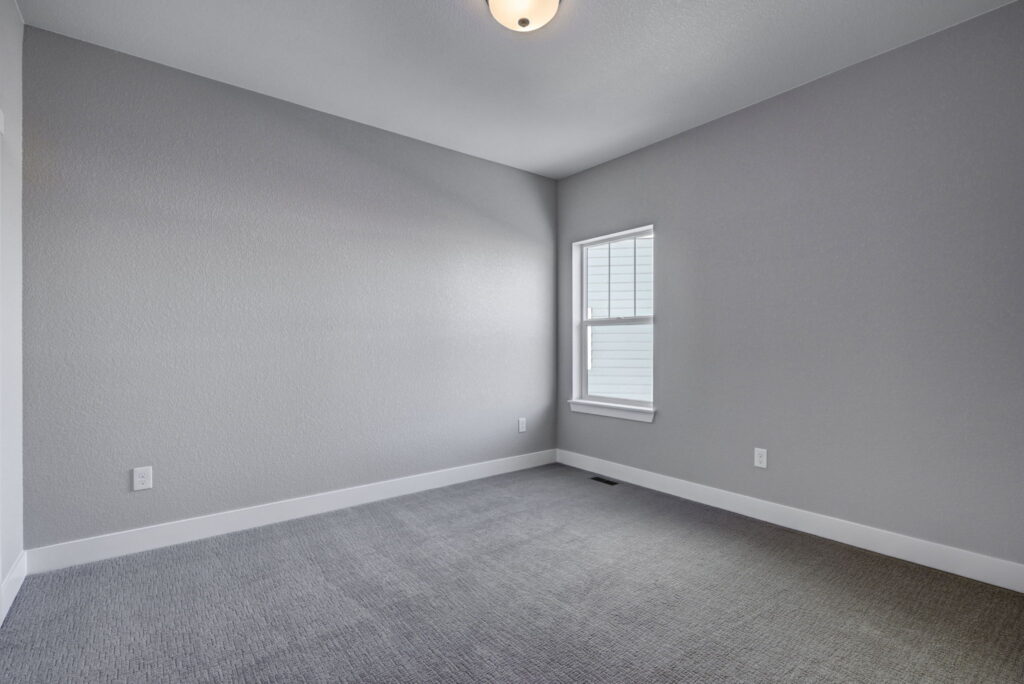 Empty carpeted room with gray walls, a small window, and ceiling light fixture.